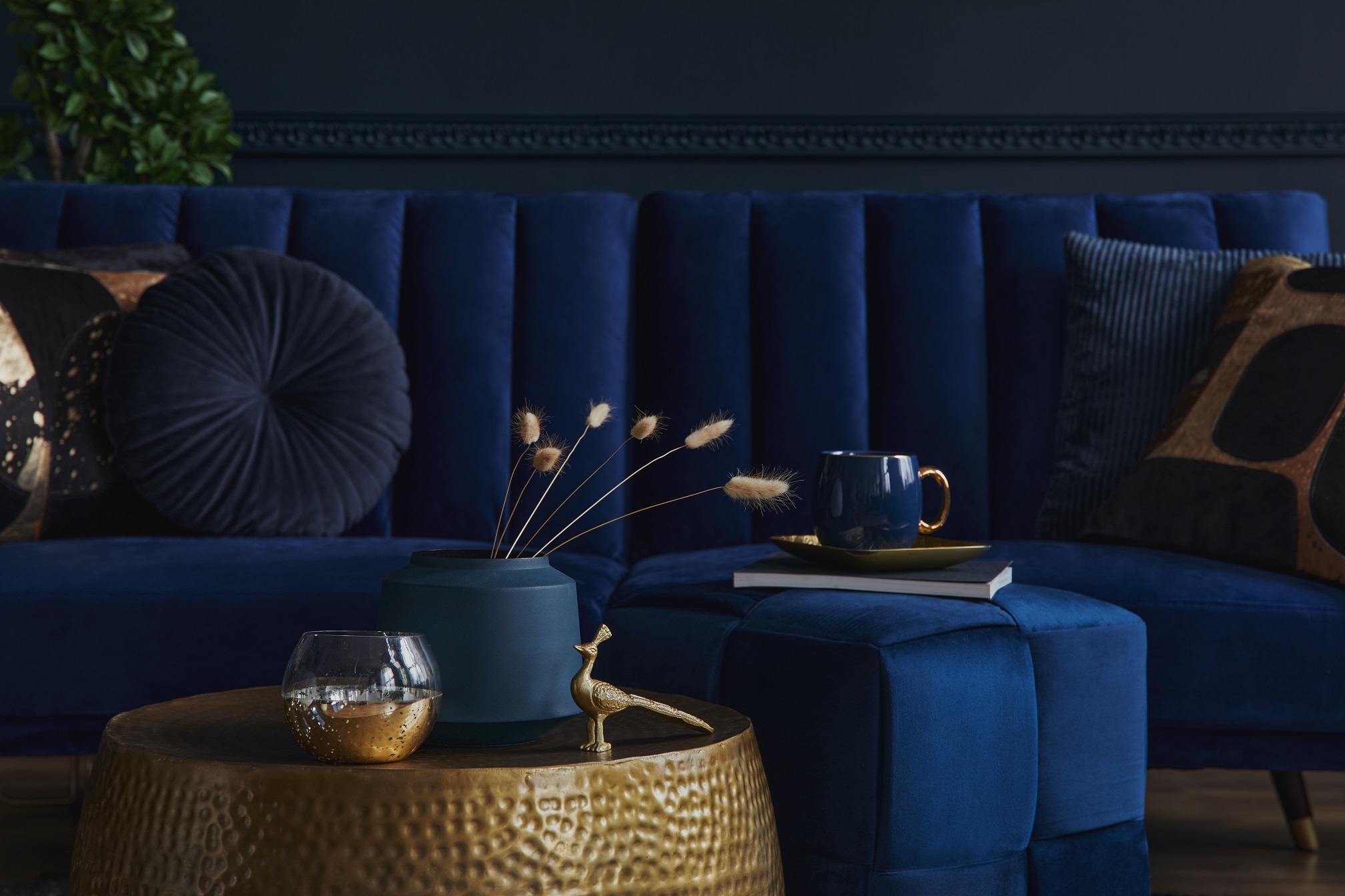 Stylish and elegant details in the glamour living room interior. Golden metal coffee table and creative personal accesories. Dark blue sofa on the background. Template. Copy space.
